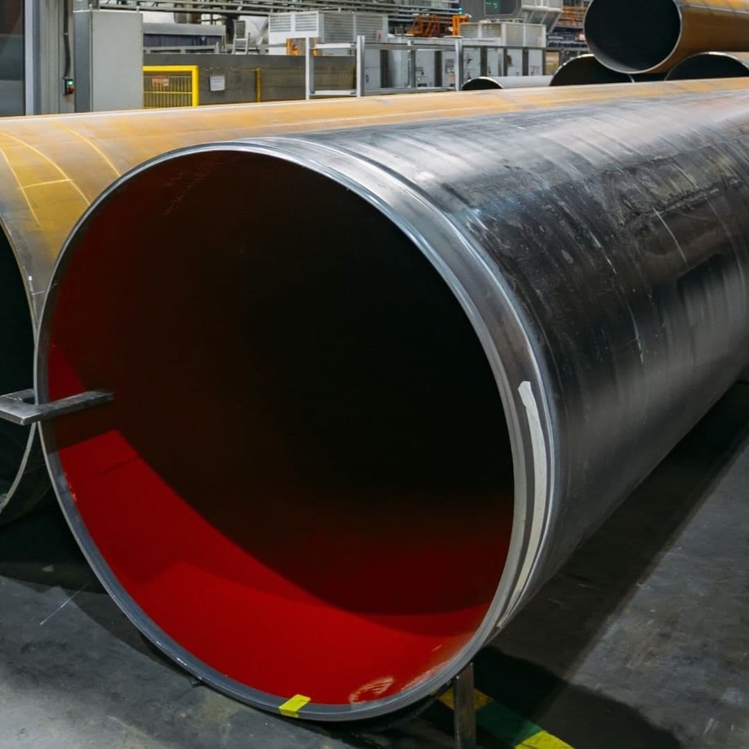 Tubos de acero grandes apilados en un entorno industrial con equipos de fondo.