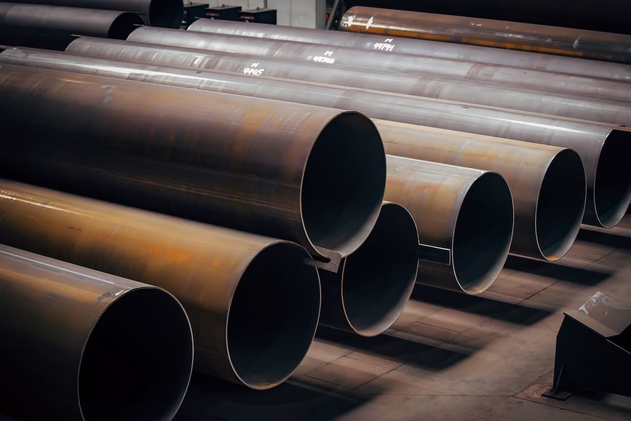 Tuberías de acero de gran diámetro apiladas en un entorno industrial, con una iluminación suave que resalta sus acabados.