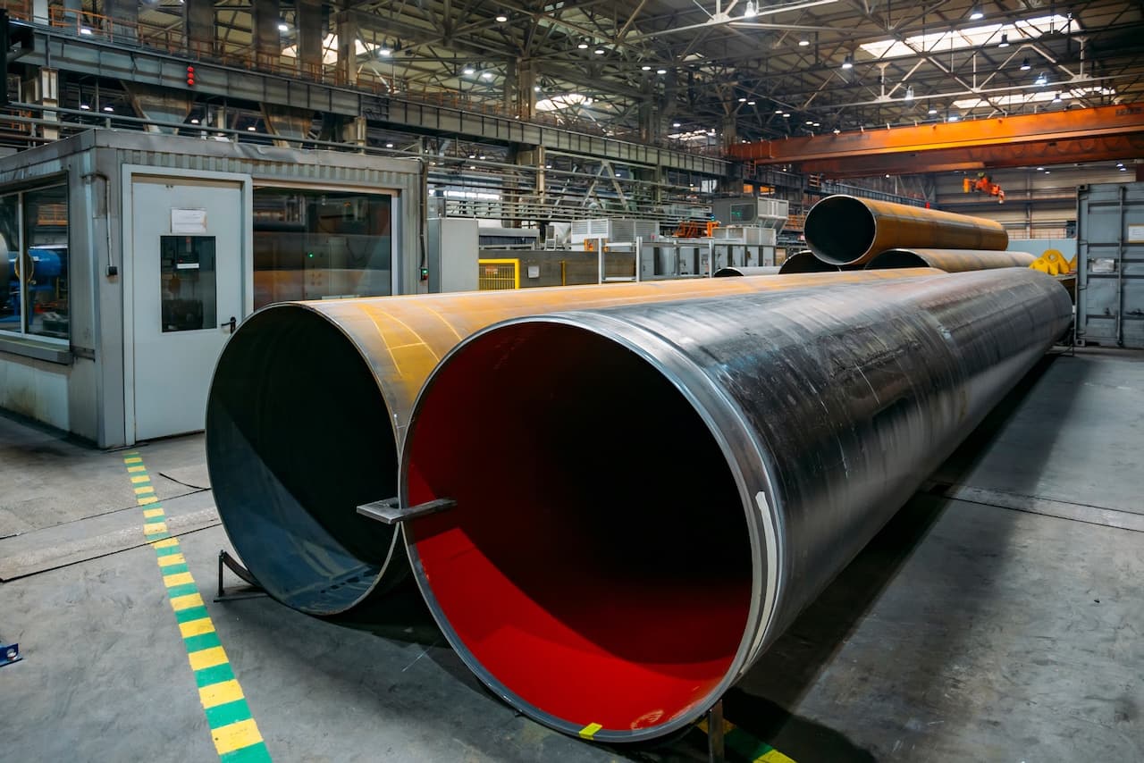 Tuberías de acero en un taller industrial, con diferentes diámetros y colores, rodeadas de maquinaria y un ambiente de trabajo bien iluminado.