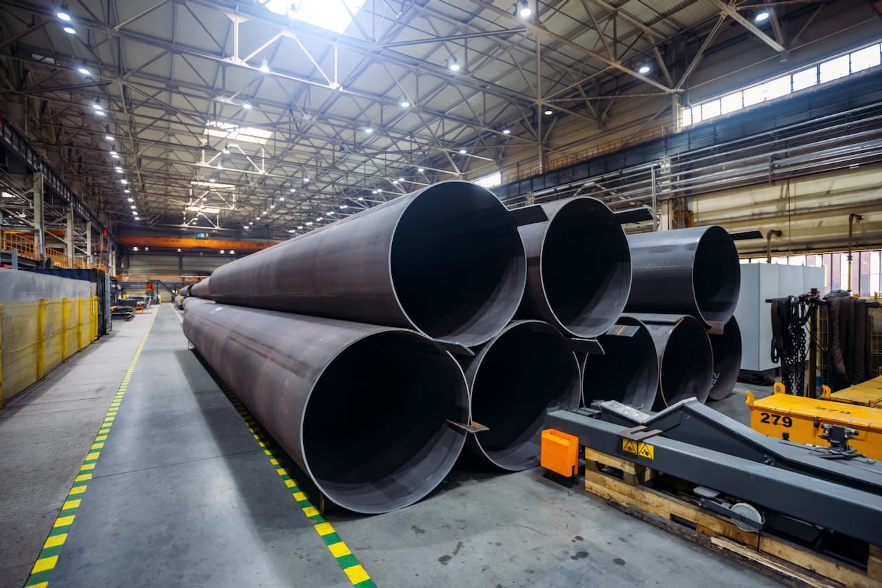 Tuberías de acero apiladas en un entorno industrial amplio y bien iluminado.