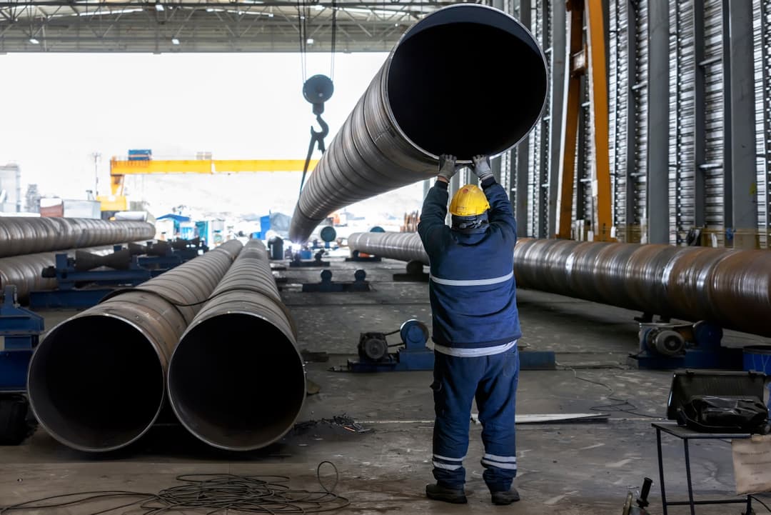 Persona descargando Tuberias gigantes de acero en un taller industrial.