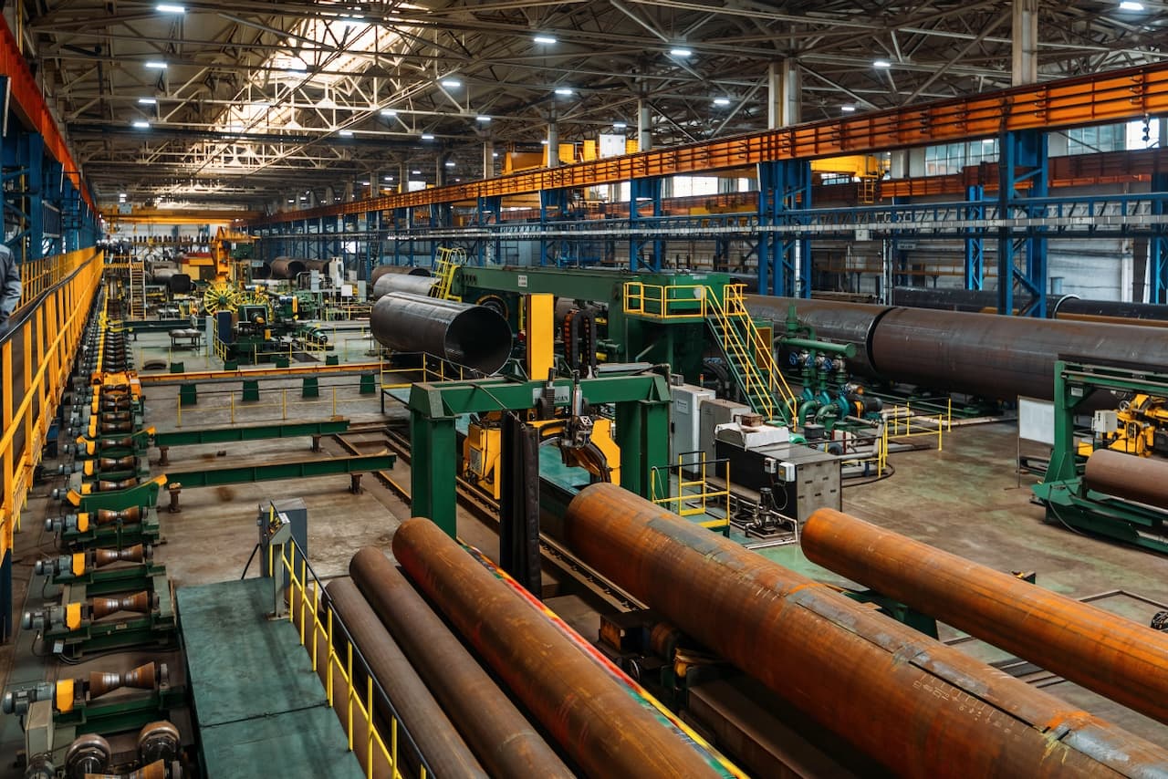 Fábrica con maquinaria y equipos para la producción de tubos de acero, con un ambiente industrial amplio y ordenado.
