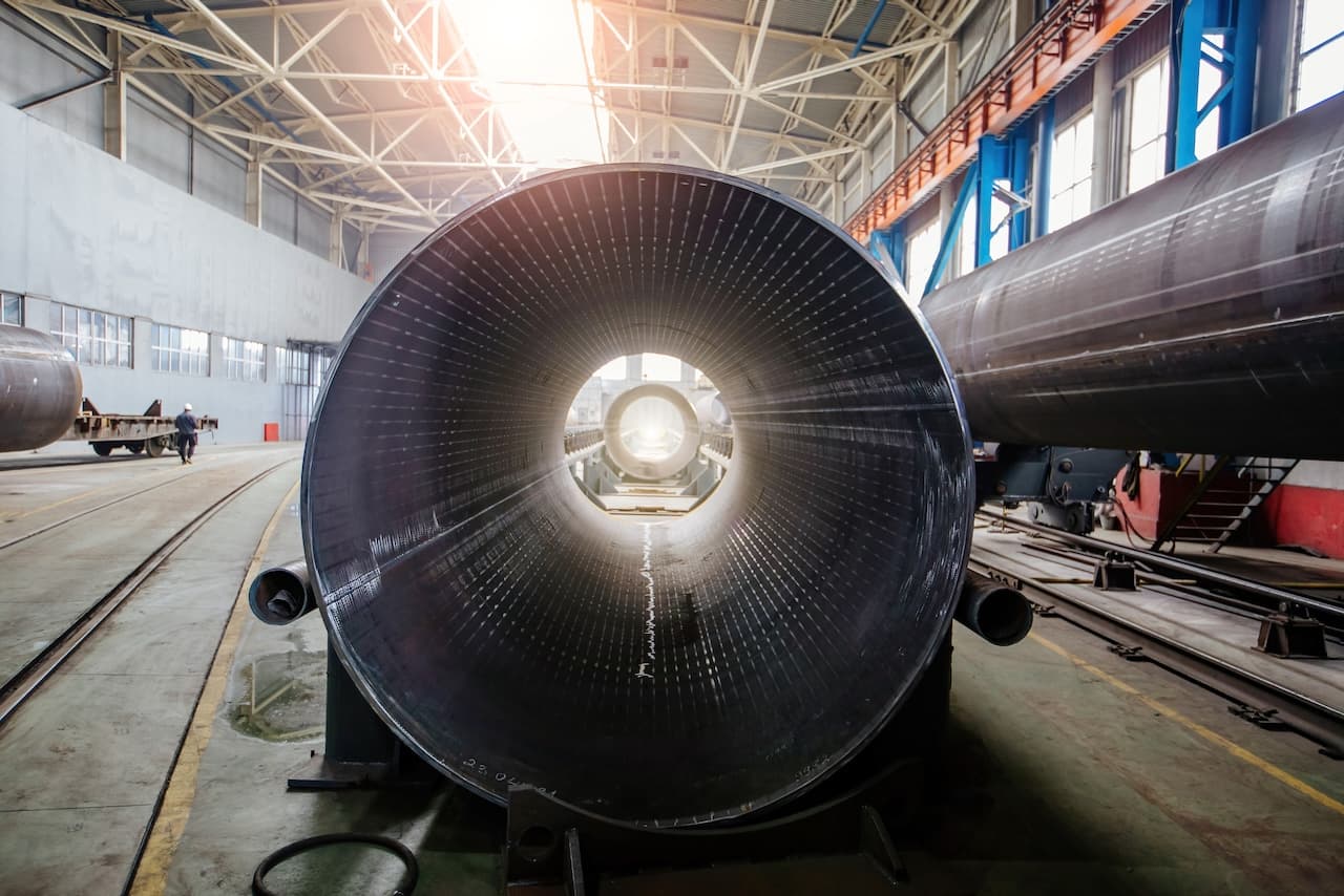 Tuberías grandes en un taller industrial, con una iluminación brillante al fondo y una persona caminando.