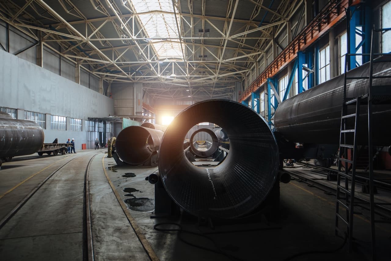 Fábrica con grandes tubos de acero en un ambiente industrial iluminado por la luz del sol que entra a través de ventanas.