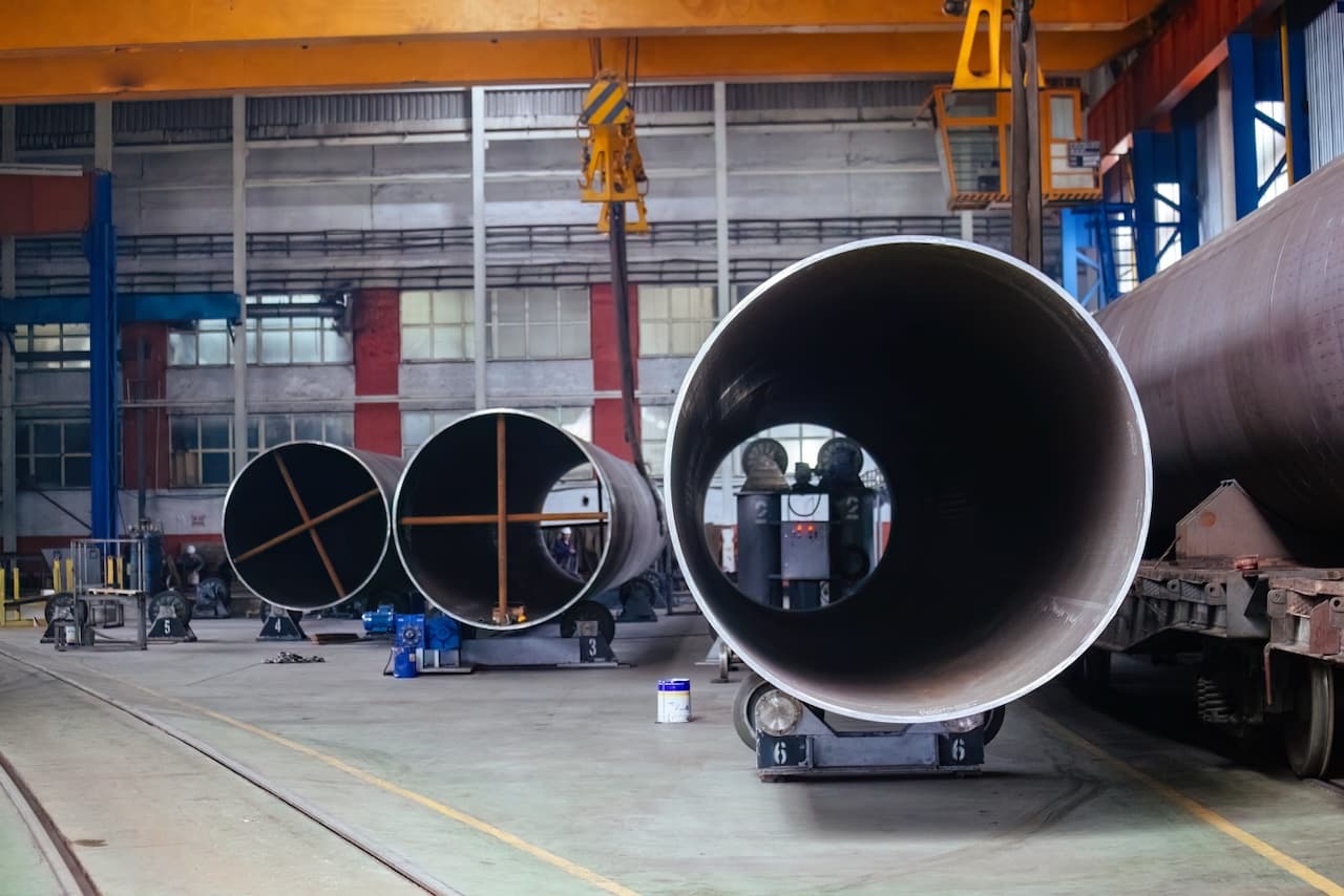 Tuberías de acero grandes en una fábrica, con un entorno industrial y maquinaria visible.