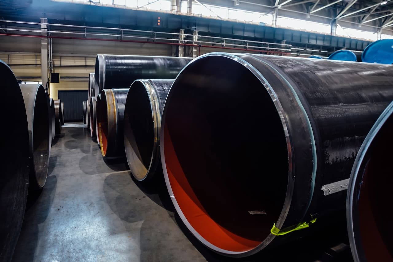 Tuberías de acero apiladas en un entorno industrial, con algunas mostrando un interior de color naranja.