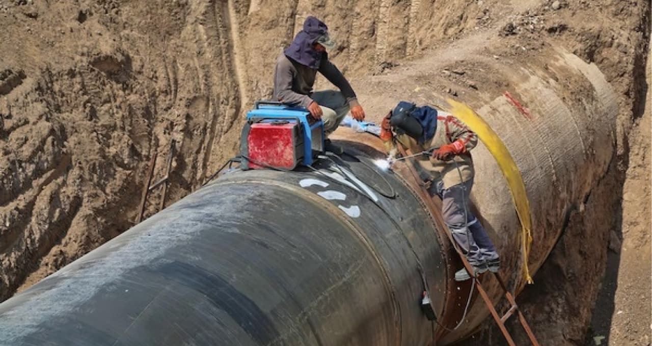 Trabajadores realizando soldadura en una tubería de acero en una zanja.