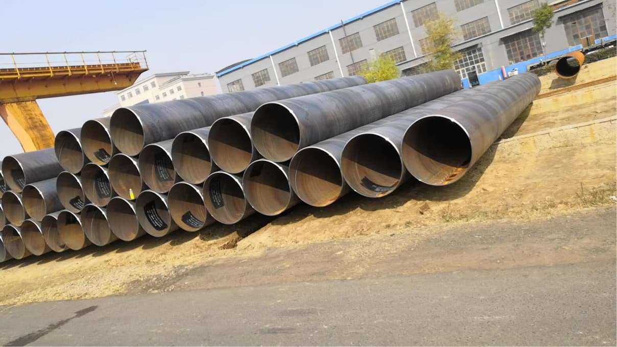 Conjunto de tuberías de acero apiladas en un terreno cercano a un edificio industrial.