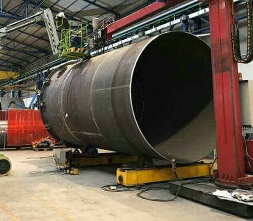 Gran tubo de acero en un taller industrial con maquinaria en el fondo.