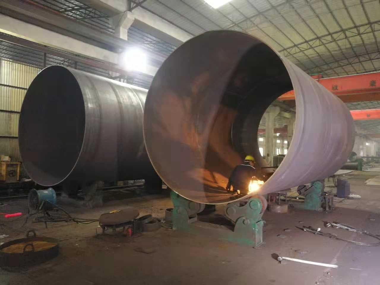 Persona soldando una tubería gigante de acero en un taller industrial.